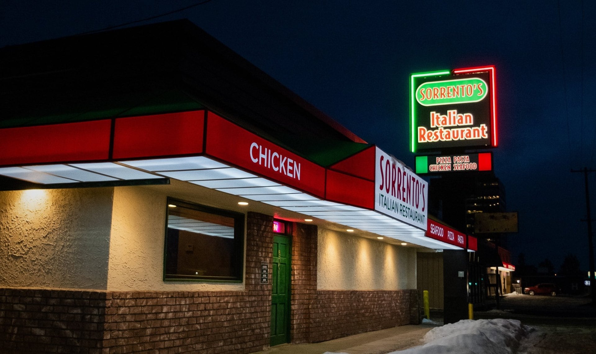 Sorrento's Restaurant storefront in Anchorage, its green neon sign glowing over a red awning at dusk